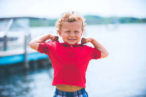 Willenskraft stärken: Ein Kind im roten T-Shirt macht eine Muskelpose